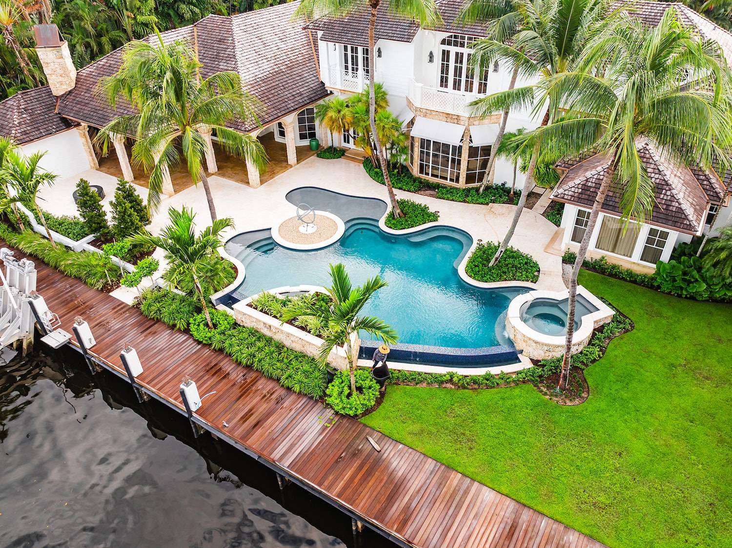 Aerial view of luxury waterfront home with pool, dock, and manicured estate landscape in Palm Beach County